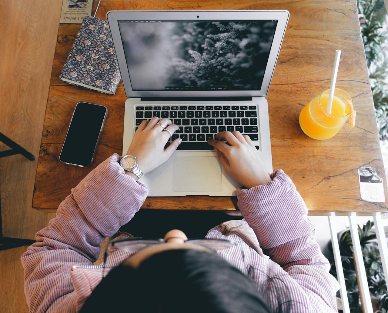 Top view of a person working on a laptop with a smartphone and juice on a wooden desk.