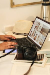 Woman working on laptop with a camera and hat on the desk, symbolizing creativity and technology.