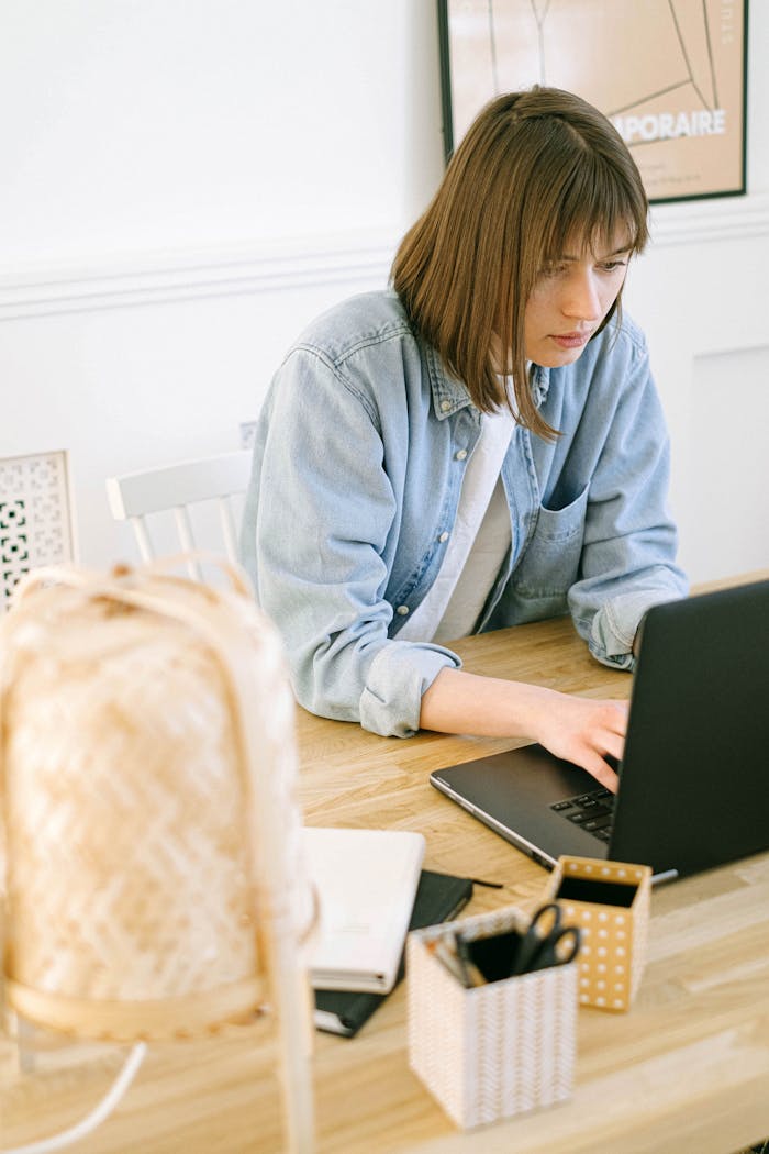 Young woman working on a laptop in a cozy home office setting, focused and engaged.